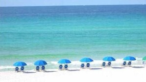 A beach with several blue umbrellas and lounge chairs. - Golf Cart! Pet-friendly! Linkside Village 435! (Miramar Beach)