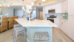 Een moderne keuken met witte kasten, een groot kookeiland met stoelen, en hangende pendelverlichting.