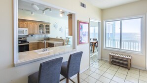 A kitchen with a large window, a dining area with two chairs, and a view of the ocean. - Gulf front! Pet Friendly! Beach House 30A Unit #2 - Gulf Front, Dune Allen Beach (Santa Rosa Beach)