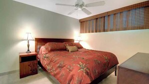 A bedroom with a bed, nightstands, a ceiling fan, and a window with blinds. - Oceanfront Escape: Kihei Surfside #211 – W/ Gorgeous Views & Grounds (Kihei, Maui)