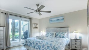 Une chambre à coucher avec un lit, un ventilateur de plafond, une table de chevet, une lampe et une vue sur l’extérieur.