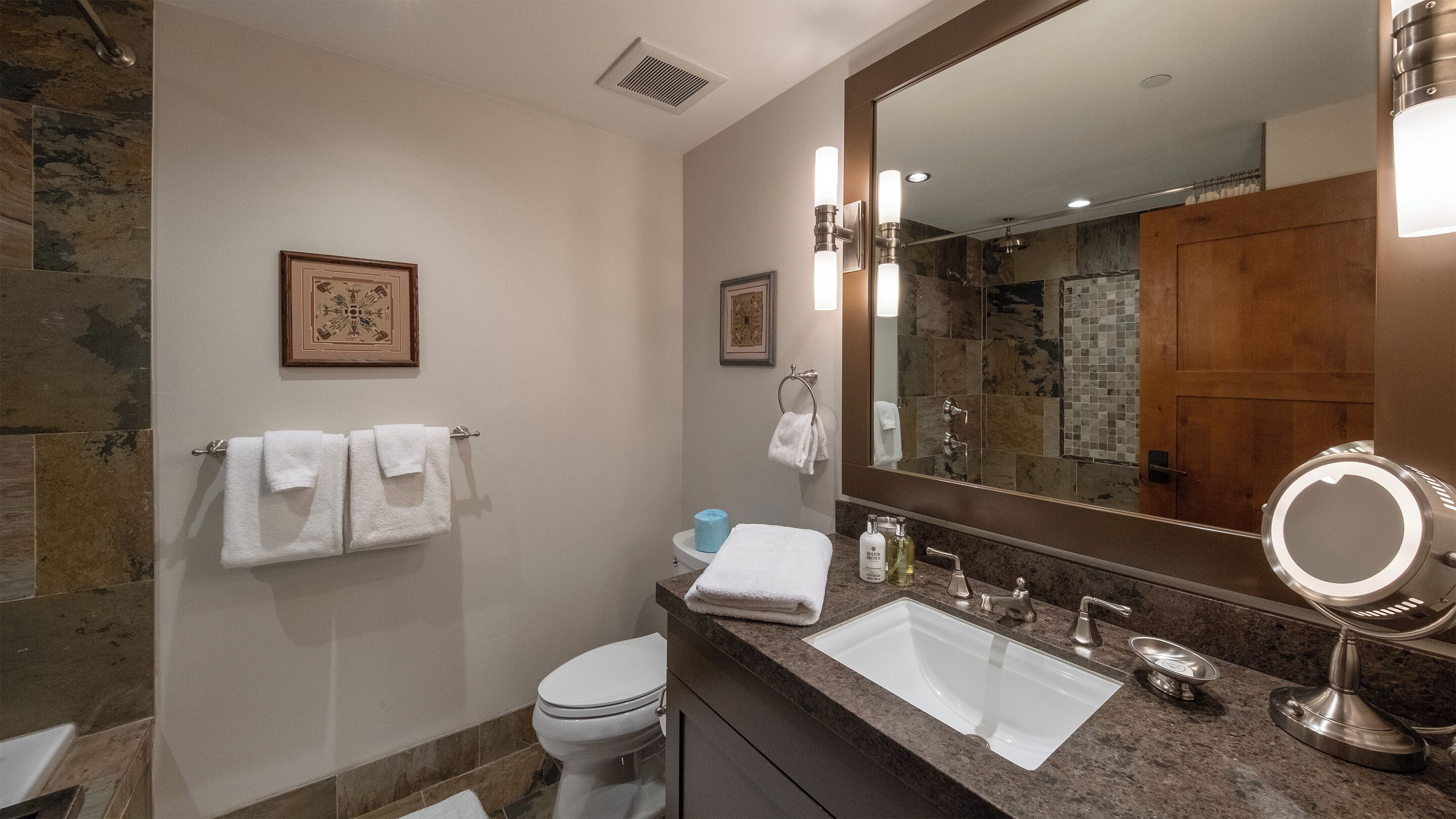 A modern bathroom with a marble wall, a large mirror, a sink, and a toilet.