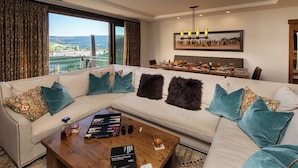 A modern living room with a large sectional sofa, a wooden coffee table, and a dining area with a chandelier.