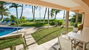Ein Poolbereich mit Meerblick, umgeben von Palmen und einer Terrasse mit Stühlen und einem Tisch.