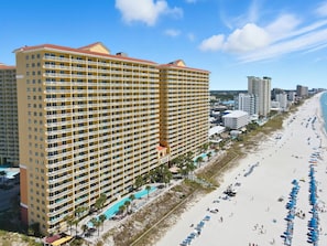 A large hotel with multiple floors and balconies, a beach with umbrellas, and a clear sky. - ☀️BeachFRONT-Free Beach Service-Calypso 1-609 East☀️ (Panama City Beach)