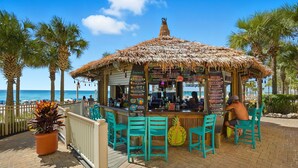 Un bar junto a la playa con techo de paja, sillas turquesas y una pizarra de menú.