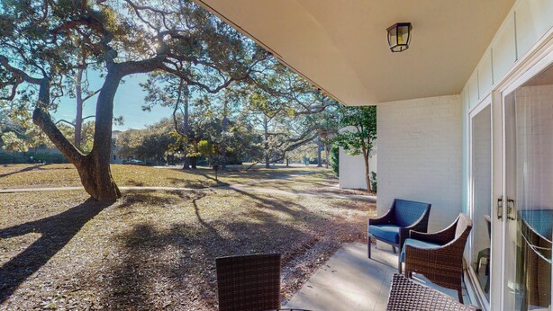 A covered patio with wicker furniture, a large tree, and a view of a park.
