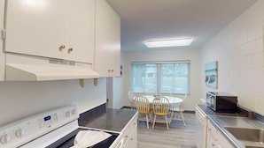 A modern kitchen with white cabinets, a built-in oven, a microwave, and a dining area with a table and chairs.