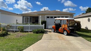 Een huis met één verdieping, met garage, een witte picket-omheining en een golfkarretje op de oprit.