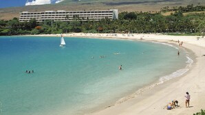 A coastal resort with a large building, sandy beach, and clear turquoise waters. - Best of Wai'ula'ula - Beautiful Decor, Ocean View, Resort Access! (Kamuela)