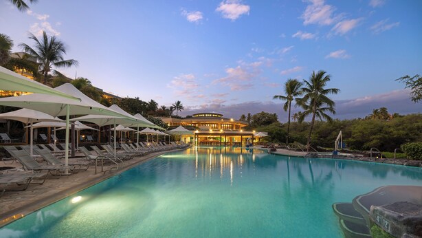 A large outdoor swimming pool with lounge chairs and umbrellas, surrounded by palm trees and a building with multiple floors and balconies. - Best of Wai'ula'ula - Beautiful Decor, Ocean View, Resort Access! (Kamuela)