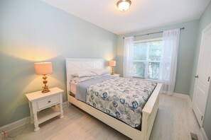 A bedroom with a bed, two bedside tables, a nightstand, a window with curtains, and a door.