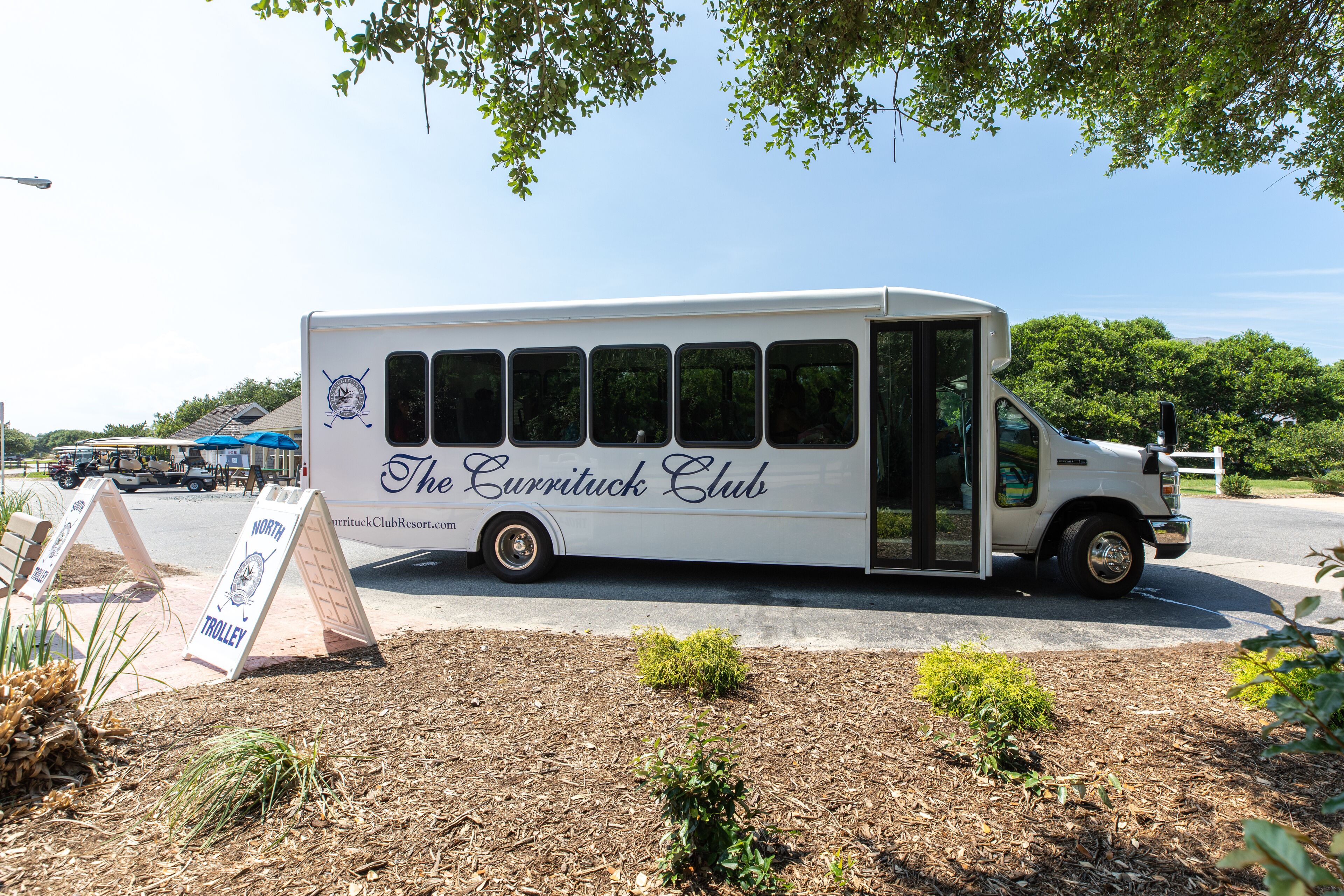 A white bus with "The Currituck Club" written on the side parked on a street.