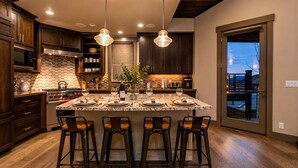 A modern kitchen with dark wood cabinets, a large island with bar stools, stainless steel appliances, and pendant lighting.
