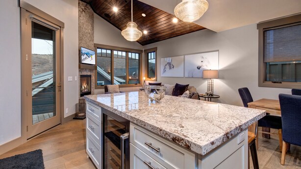 A modern kitchen with a large island, wooden ceiling, and large windows.