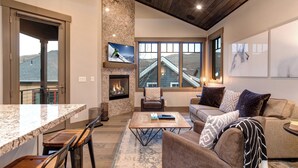 A spacious living room with a fireplace, a large window with a view, a comfortable sofa, and a dining area with a granite countertop.