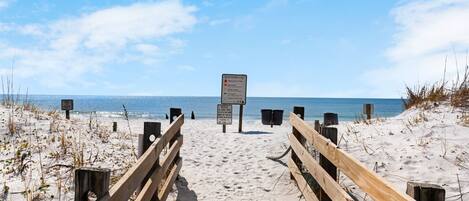 Un muelle de madera que conduce a una playa con banderas de advertencia y un cartel que indica prohibido bañarse.