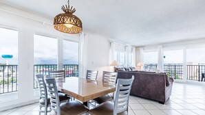 Ett rymligt matområde med ett träbord och metallstolar, en soffa och ett stort fönster med utsikt över staden.