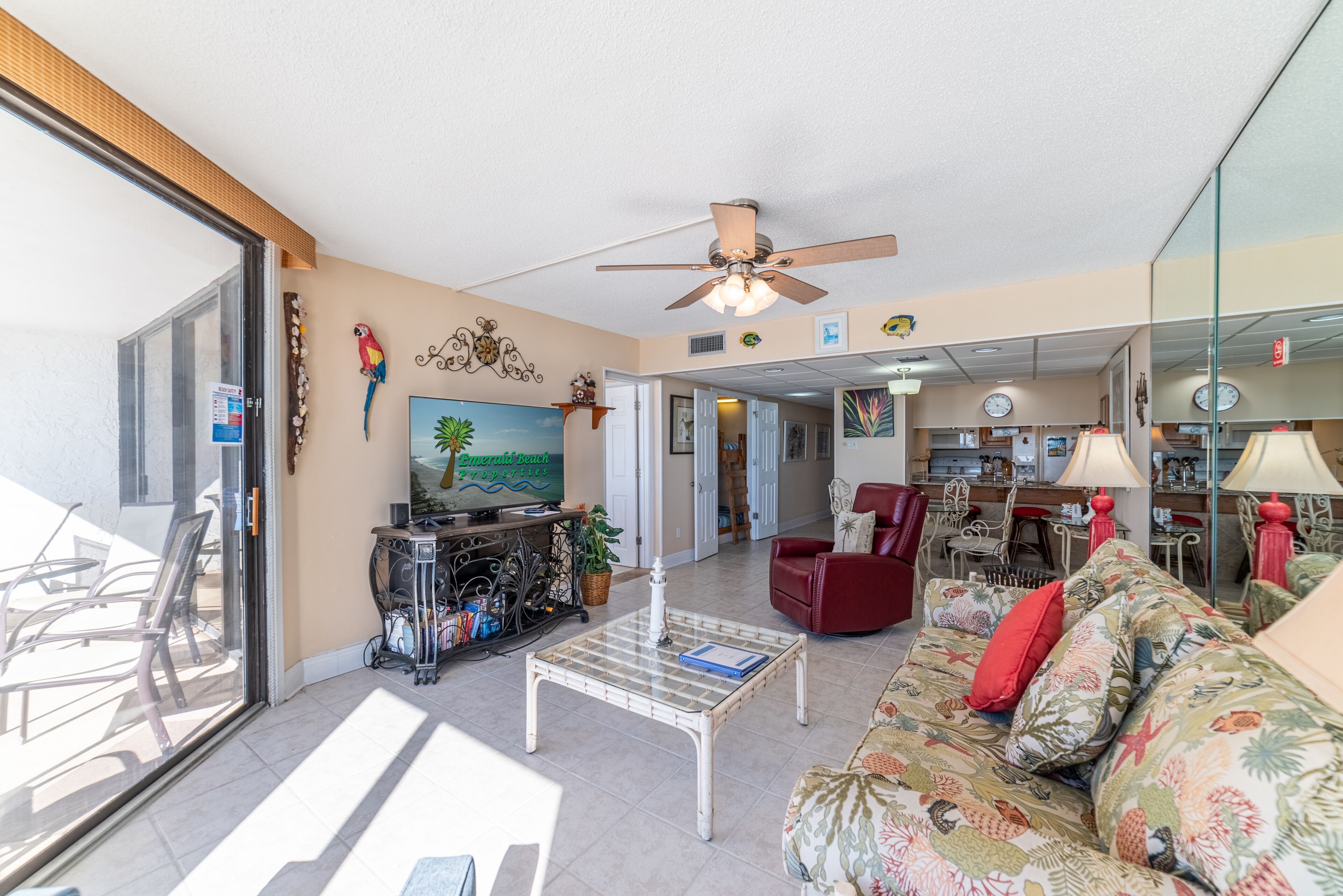 A spacious living area with a ceiling fan, a television, a coffee table, and a sofa with floral cushions.