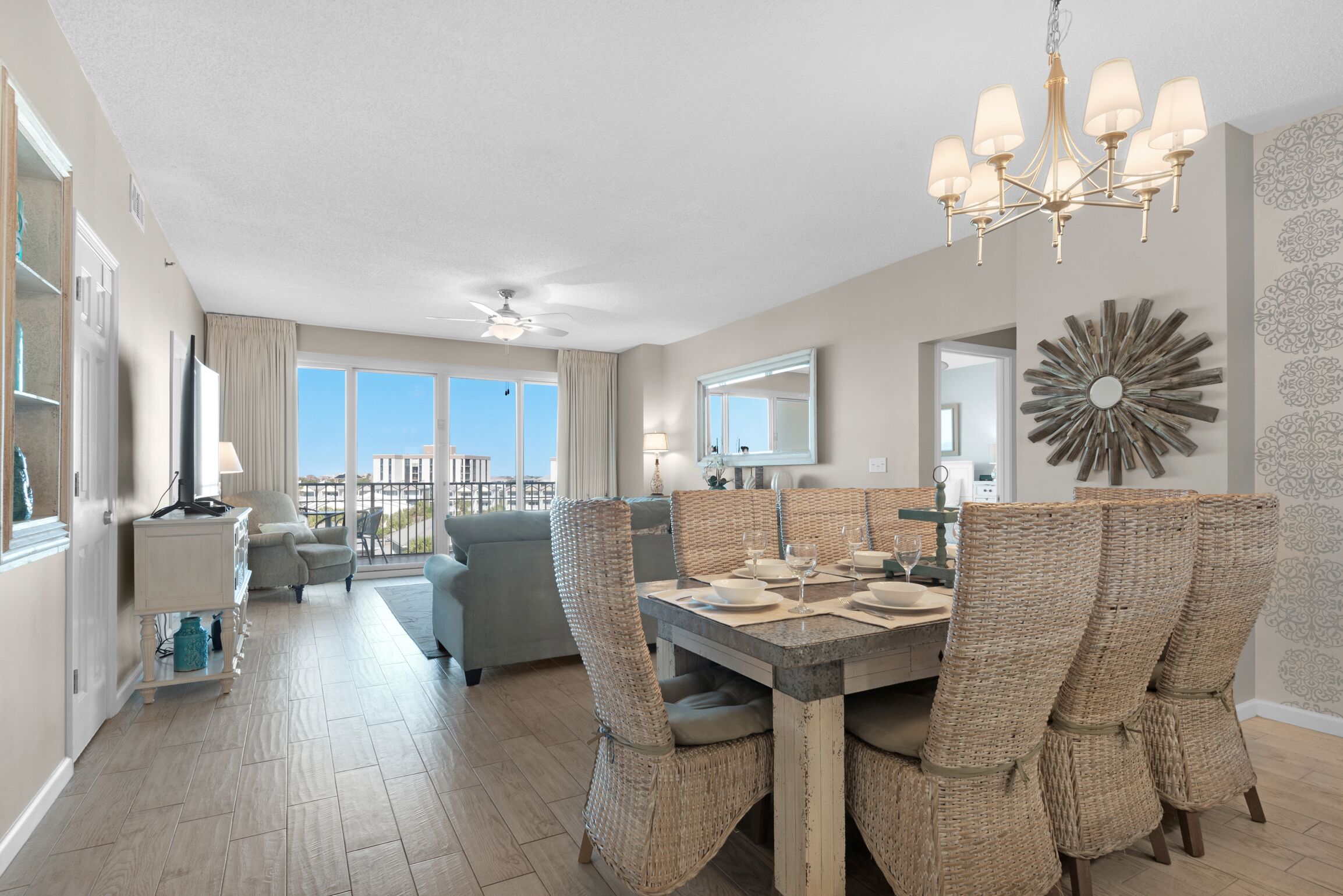 A spacious dining area with a high table and wicker chairs, a chandelier, and a large mirror on the wall.