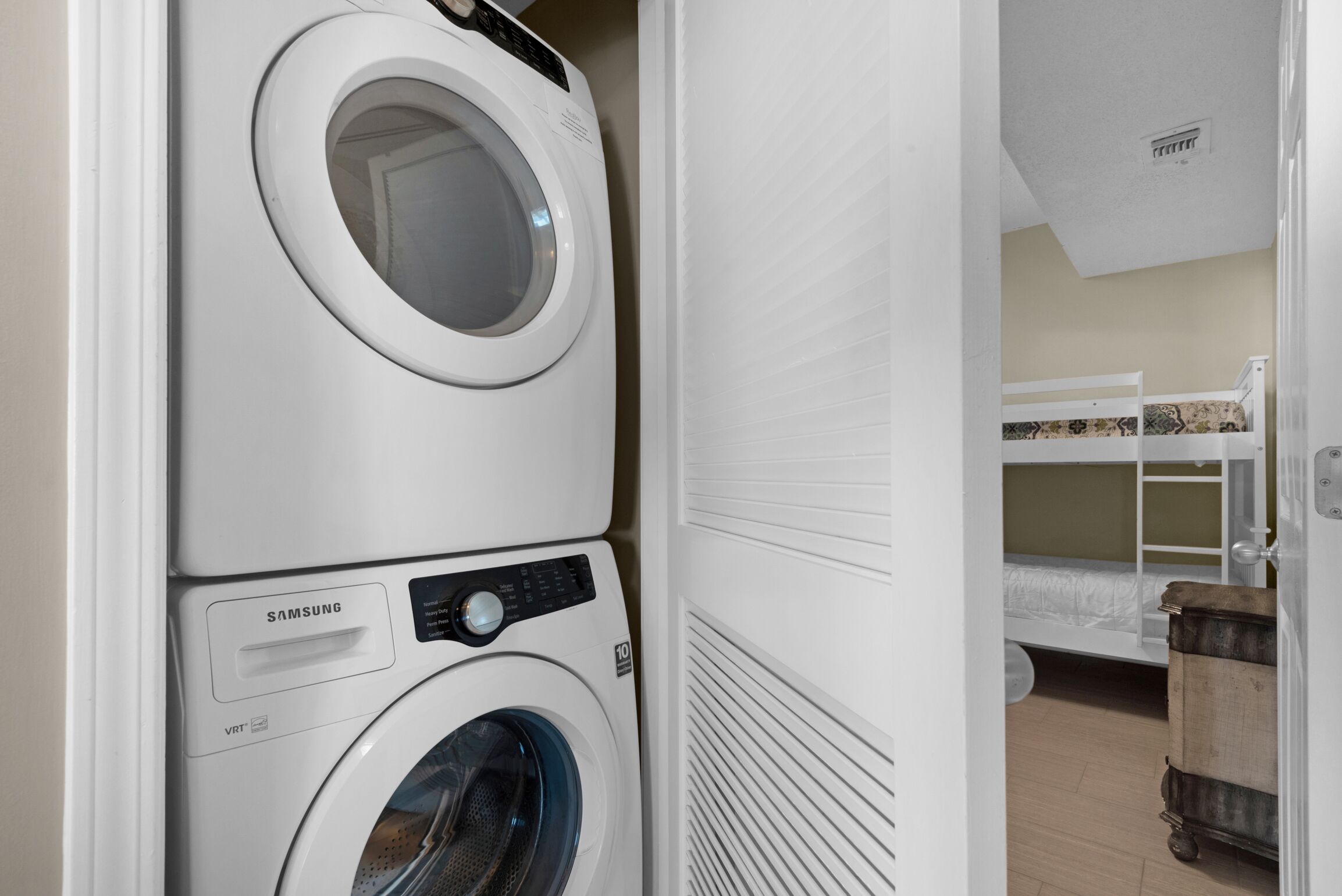 A laundry room with stacked washers and dryers, a bunk bed, and a wooden dresser.