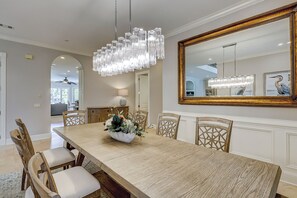 Un comedor con mesa de madera, sillas, una lámpara de araña y un espejo grande.