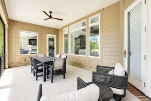 Une terrasse couverte avec une table et des chaises, un ventilateur de plafond et de grandes fenêtres.
