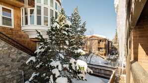 Un espacio exterior cubierto de nieve con un muro de piedra, una escalera de madera y un árbol cargado de nieve.