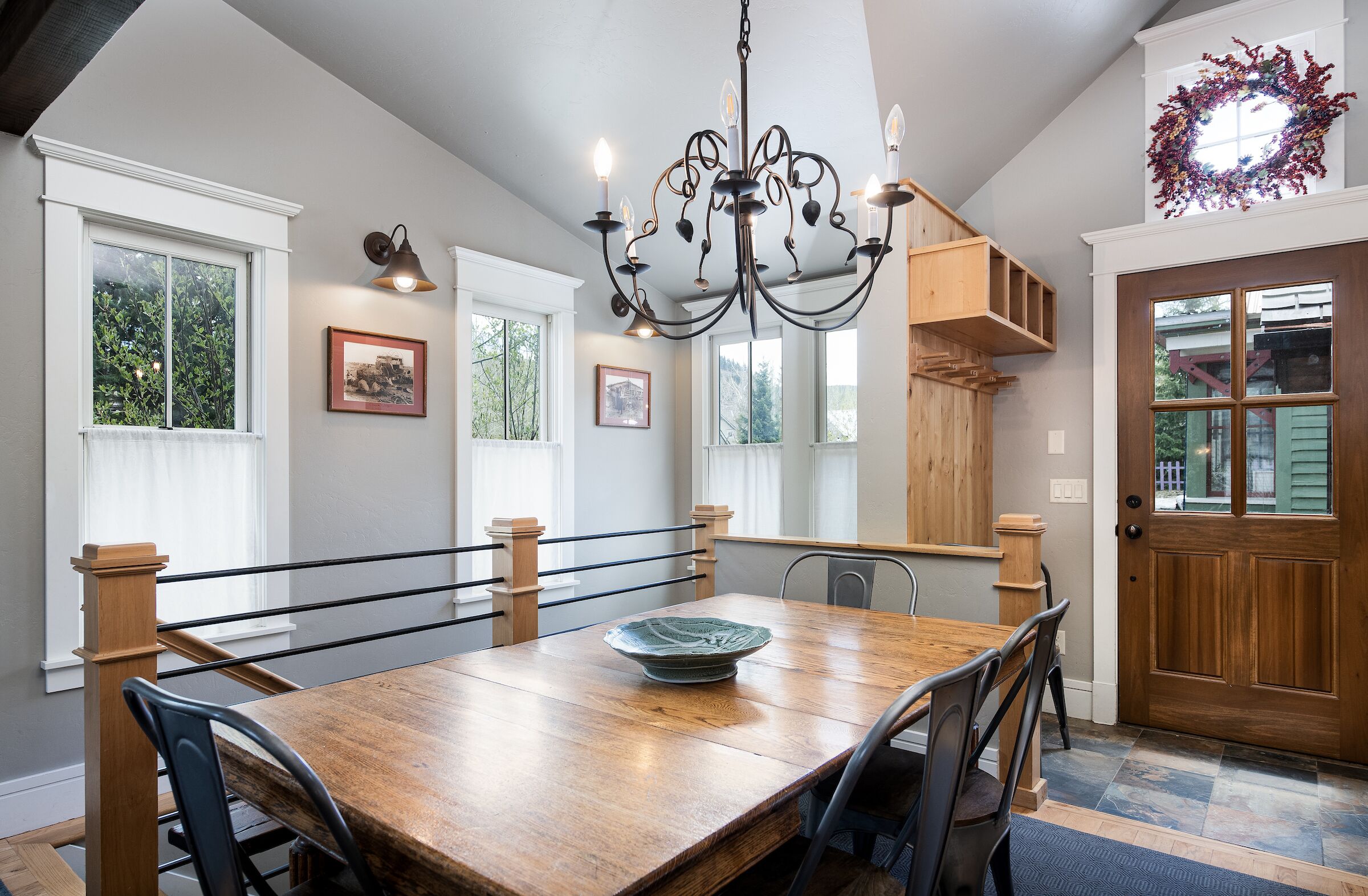 A dining area with a wooden table, chairs, a chandelier, and a large window with a view of greenery.
