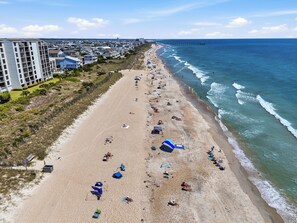 A beach with people sunbathing, umbrellas, and a pier in the background.
