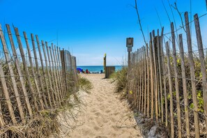 A sandy beach path with wooden fences and a clear blue sky.