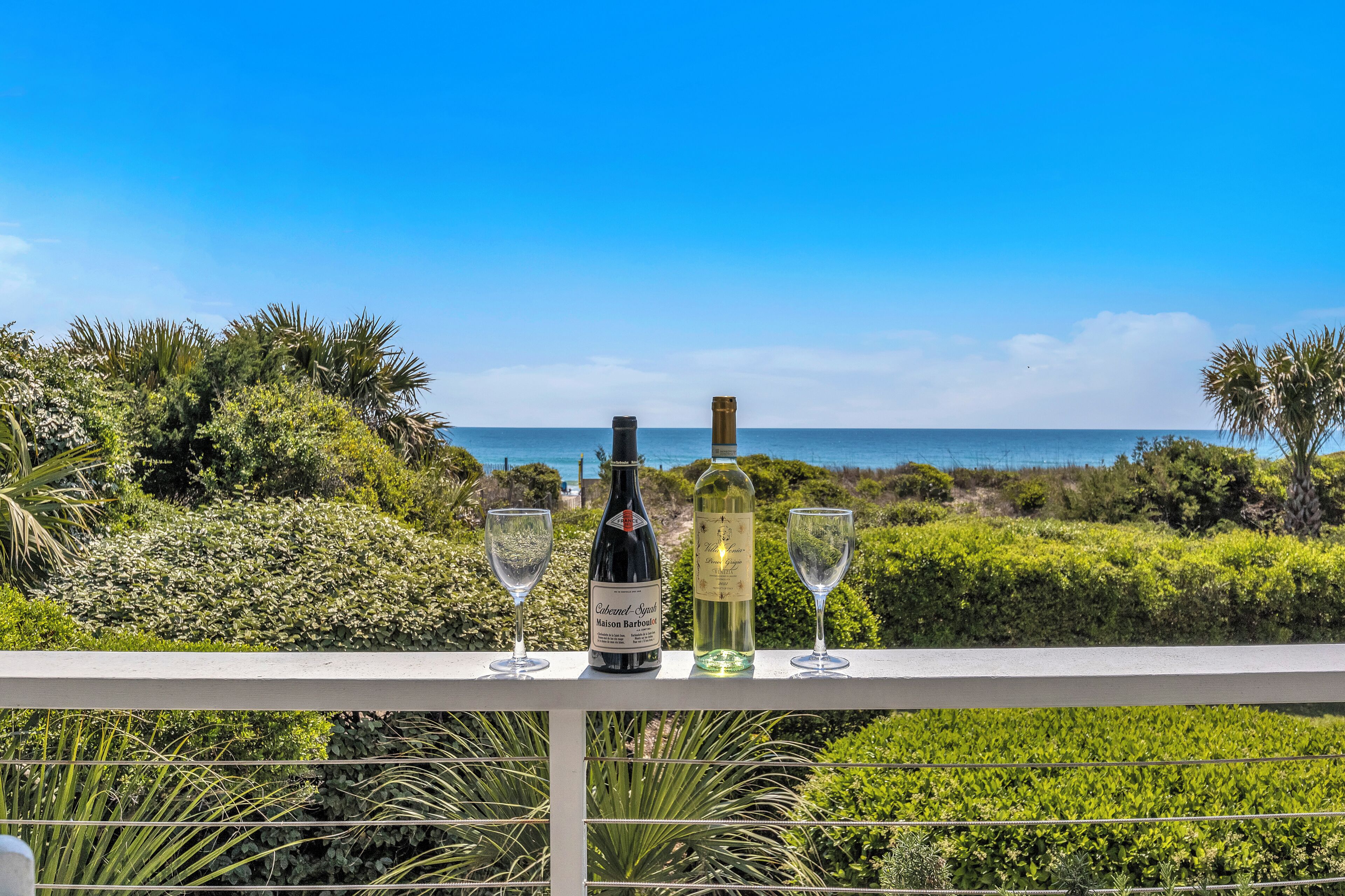 A balcony with a view of the ocean, a bottle of wine, and two glasses.