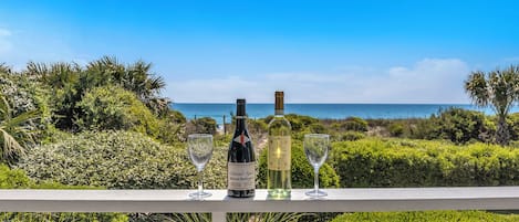 A balcony with a view of the ocean, a bottle of wine, and two glasses.