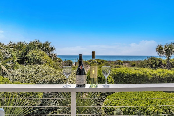 A balcony with a view of the ocean, a bottle of wine, and two glasses.