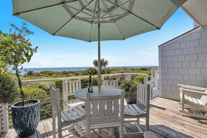 A wooden deck with a table and chairs, a potted plant, and a view of the ocean.