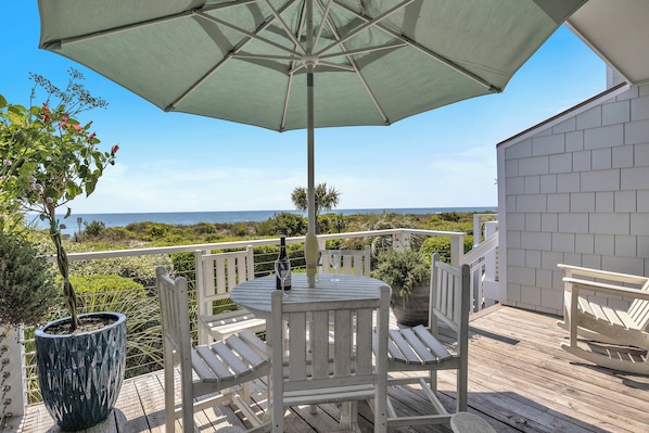 A wooden deck with a table and chairs, a potted plant, and a view of the ocean.