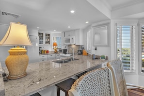 A kitchen with white cabinets, a granite countertop, a sink, a microwave, and a large woven lamp.