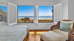 A bedroom with a large window, a bed, a chair, and a view of the beach. - Beautiful ocean front townhome in the heart of WB! (Wrightsville Beach)