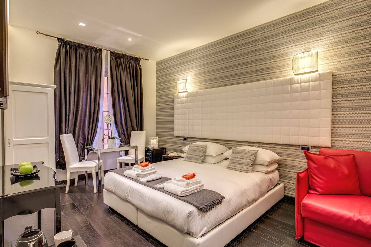 Une chambre d’hôtel moderne avec un grand lit, un bureau, un canapé rouge et une vue sur la ville.