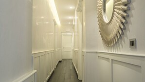 A narrow hallway with white walls and a wooden floor. A large, sunburst mirror is mounted on the right wall. - Navona Living Rome (Rome)