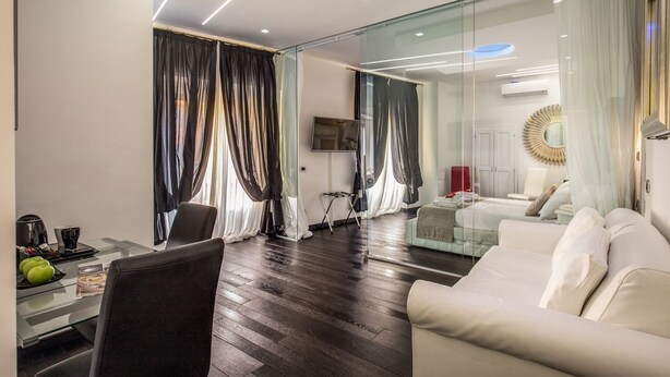 A modern living room with a glass partition, a sofa, a dining area with a glass table, and a television mounted on the wall. - Navona Living Rome (Rome)