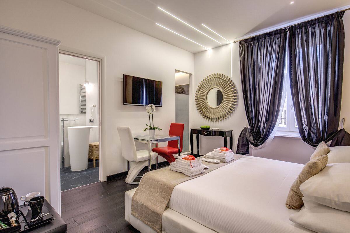 Une chambre d’hôtel moderne équipée d’un lit, d’un bureau, d’une chaise, d’une télévision et d’une salle de bain visible à travers une porte ouverte.