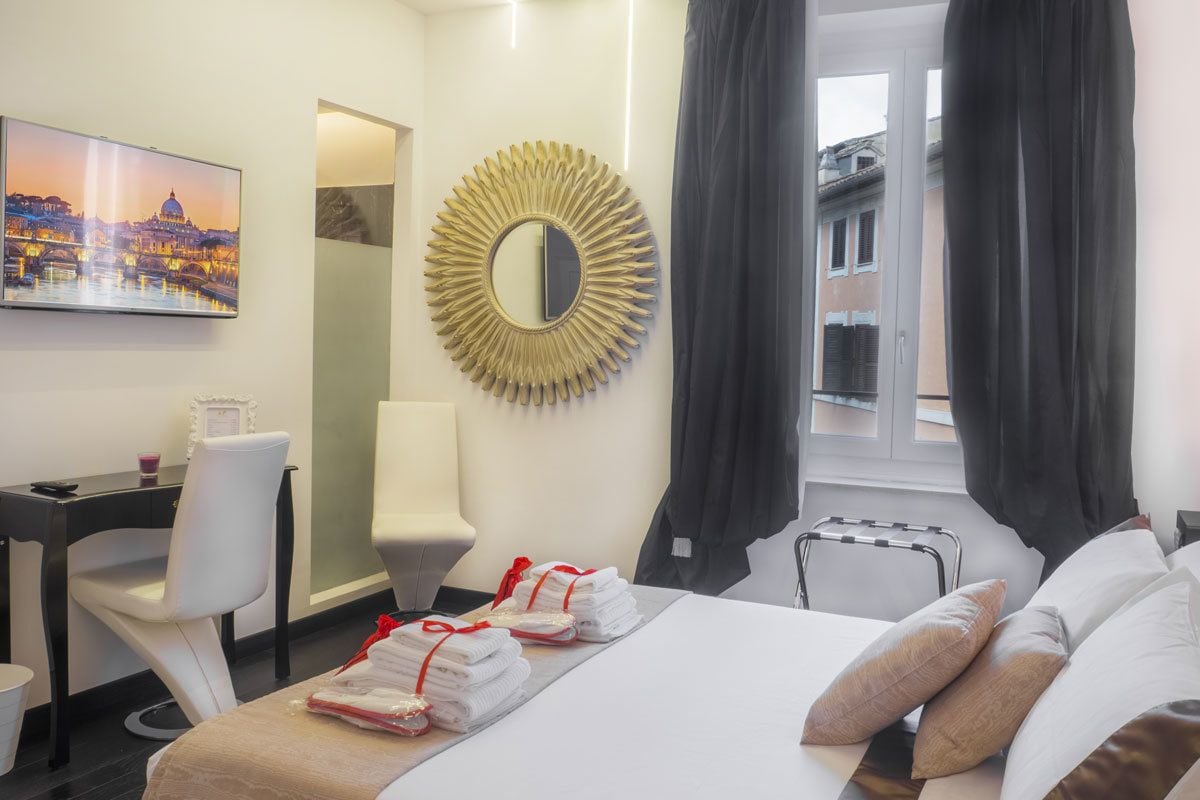 A hotel room with a bed, a desk, a chair, a large mirror, and a view of a cityscape through the window.