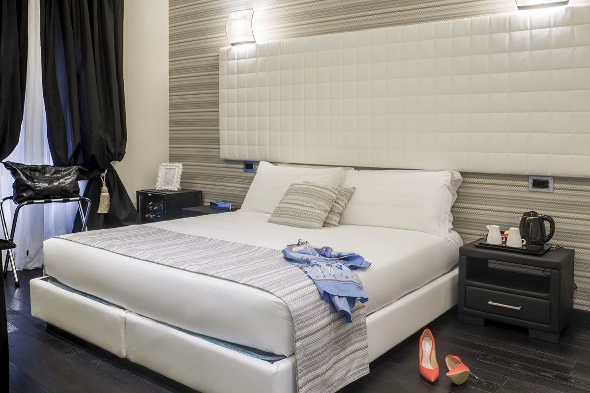 Un dormitorio moderno con una cama grande, una mesita de noche con hervidor y una mesita de cabecera con lámpara.