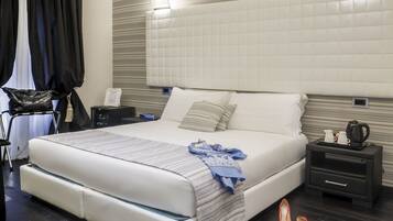 Un dormitorio moderno con una cama grande, una mesita de noche con hervidor y una mesita de cabecera con lámpara.