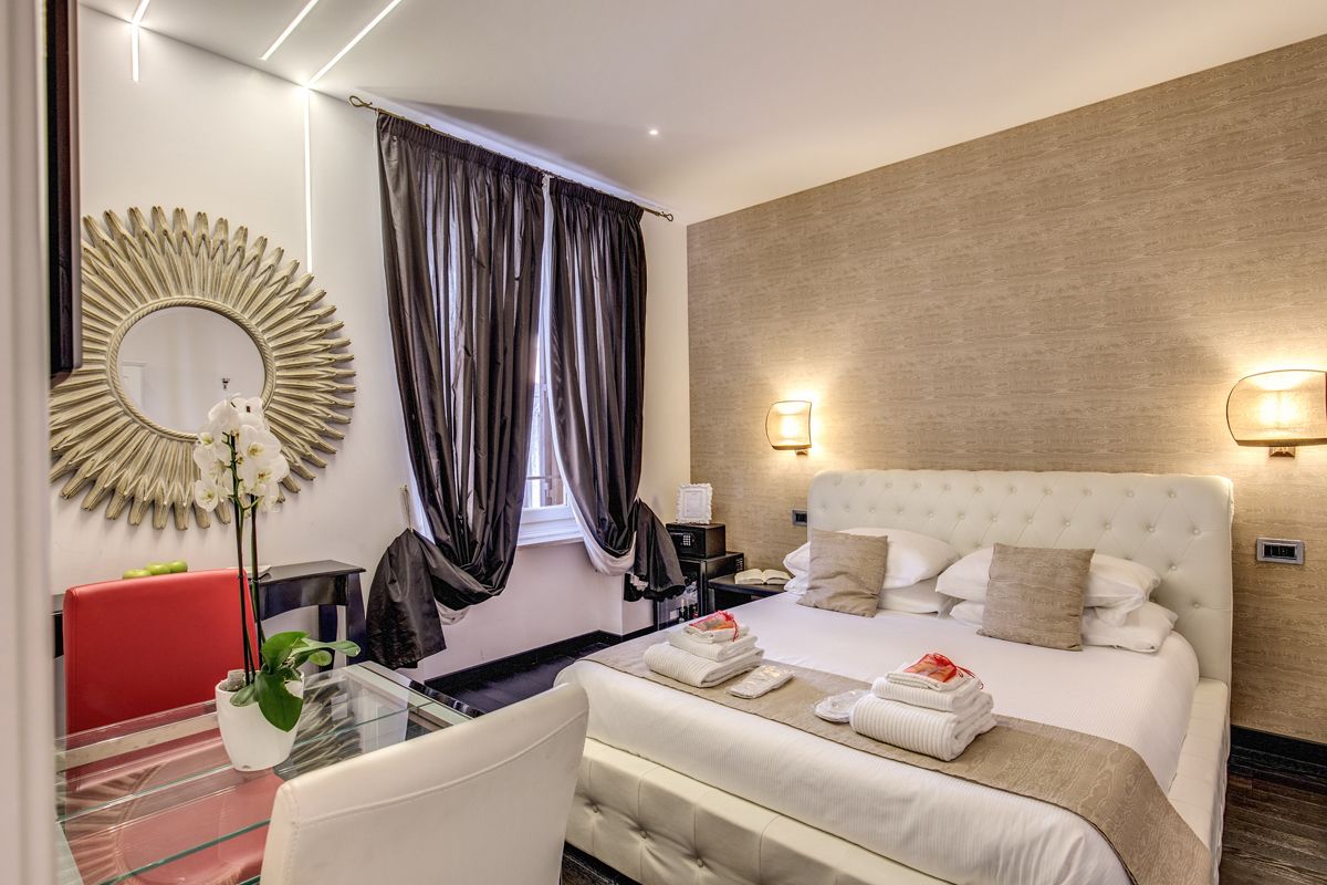A hotel room with a large bed, a round mirror, a red chair, a glass table, and a potted plant.