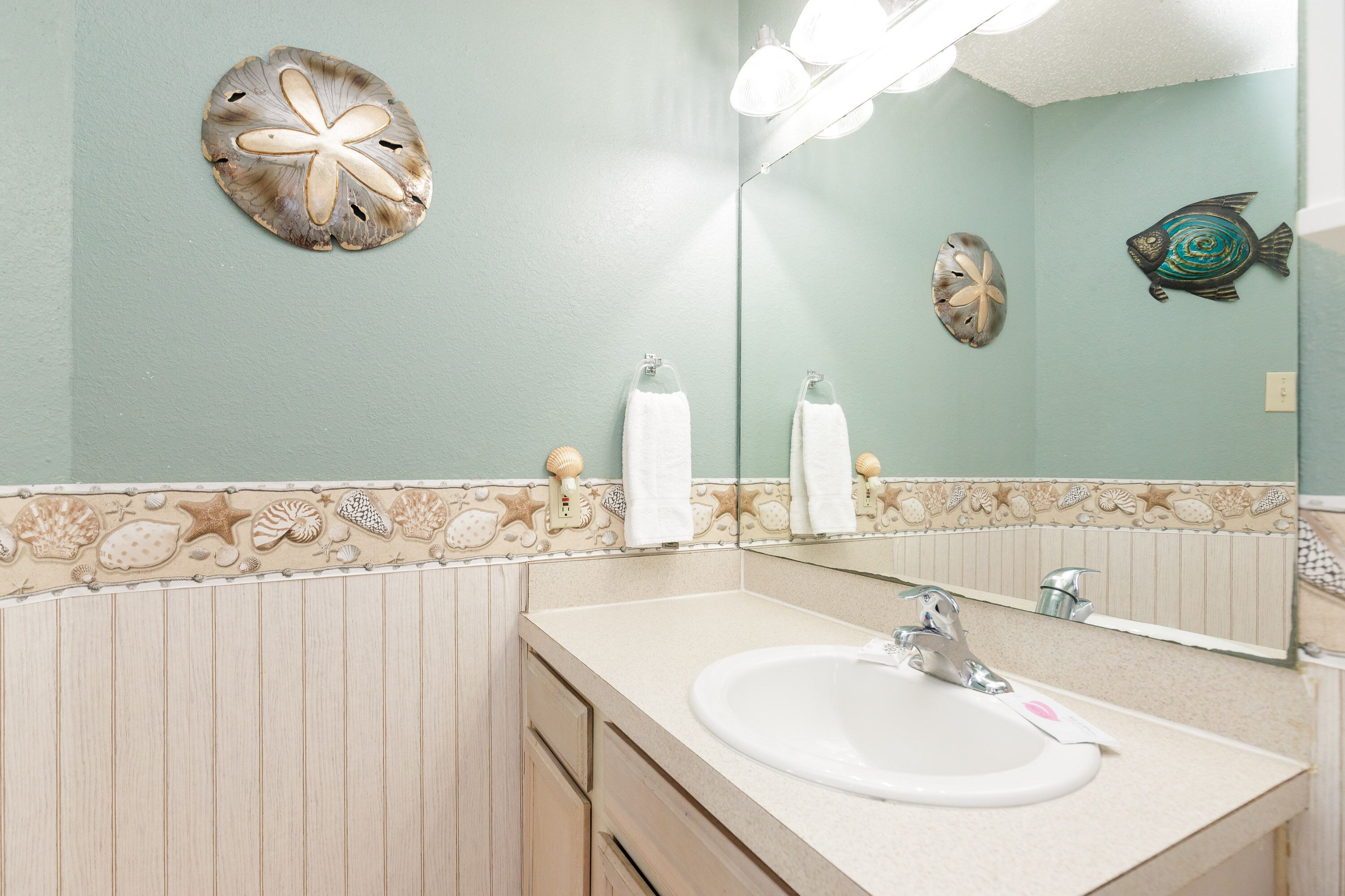 A bathroom with a sink, mirror, and decorative shells on the wall.