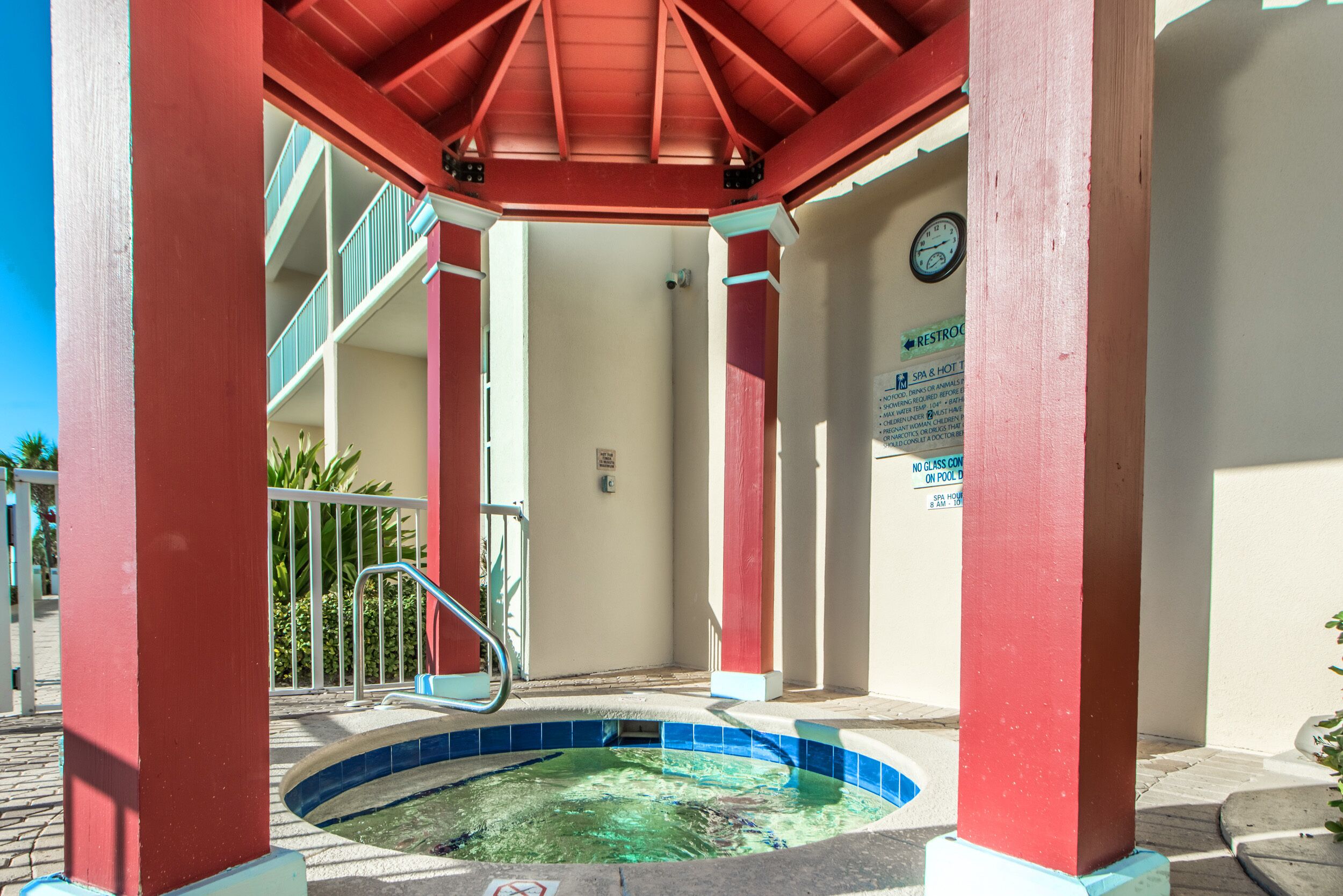 Ein überdachter Poolbereich mit rotem Dach, einem blau gefliesten Pool und einer Treppe, die zu einer oberen Ebene führt.