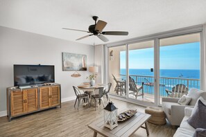 Relax in this stylish living room with a flat-screen TV, comfortable seating area, and dining table, offering a view of the ocean from the balcony.