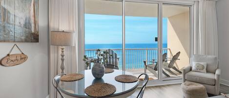 A dining area with a glass table, chairs, and a view of the ocean through large sliding doors.